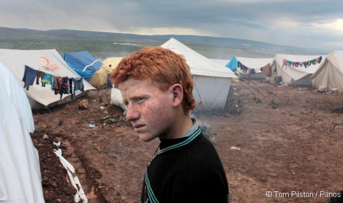 A red haired boy in Atma refugee camp on the Turkish Syrian border inside Syria. The onset of winter has worsened the living conditions in the camp with mud, cold and poor sanitation adding to the refugees' misery. Photo: Tom Pilston / Panos